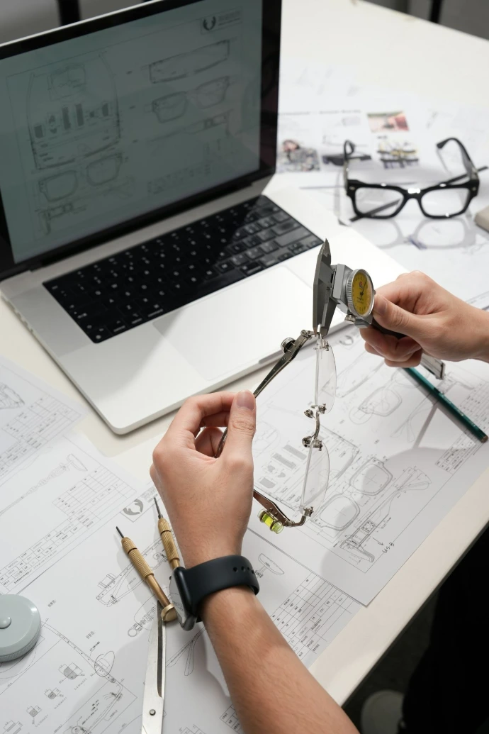 Hands measuring eyeglasses with calipers on desk